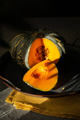 Ripe cut pumpkin still life on a tray in the rays of harsh light. Thanksgiving Still Life. Holiday festival concept. Vertical orientation.