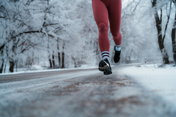 Person's legs moving along a snow covered road lined with frost dusted trees, showcasing an active...