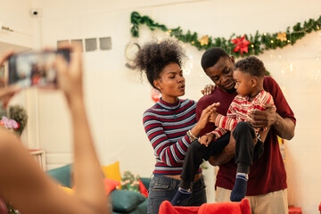 Happy Black family taking a photo with a smartphone during a Christmas celebration at home. A mother and father pose with their child. A joyful holiday moment of togetherness