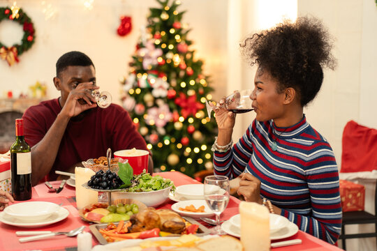 Black couple drinking wine at a festive Christmas dinner table filled with holiday food. A romantic seasonal moment of celebration, togetherness, and fine dining at home - Powered by Adobe