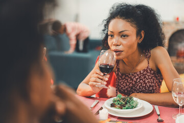 African American woman enjoying red wine and a salad during a Christmas dinner with friends or family on witnter holiday. Relaxing lifestyle at home