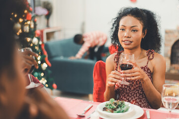 A beautiful Black woman enjoying wine and conversation during a Christmas dinner with family or friends at home. The joy of celebration and togetherness on holiday season