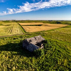 Drone view of a decaying house amid fields and a wide blue sky