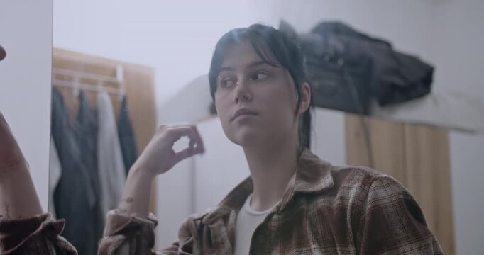 Young woman checking her reflection in a mirror at home. She adjusts her hair and clothing, preparing for her day.
