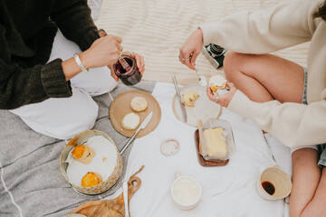 Two people are sitting on a blanket and eating food. One of them is holding a camera. Scene is relaxed and casual