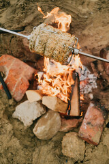Fototapeta premium A skewer of meat is being cooked over a fire, with the flames reaching high into the air. The meat is being cooked slowly and evenly, with the heat from the fire searing the outside