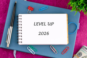 A vibrant workspace features a colorful notebook open to reveal the words Level Up 2026, surrounded...