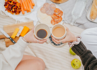 Two people holding cups of coffee and a plate of food. Scene is relaxed and casual