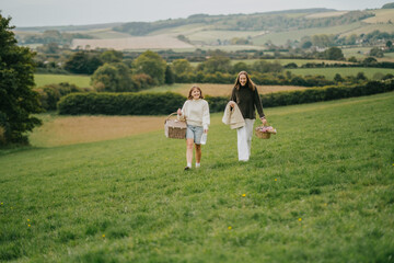 Fototapeta premium Two women walking in a field with baskets and flowers