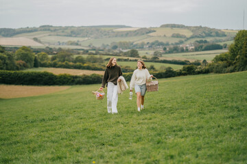 Two women walking in a field with baskets. One of them is carrying a bottle