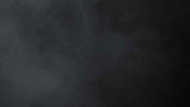 A heavy, dense cloud of white smoke or fog rolls slowly from the top left corner, creating a thick, atmospheric texture on a black background