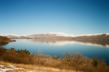 Vintage Film Photo: Epic Mountain Lake Landscape. Small Boats on Blue Water Below Distant Snow-Capped Peaks. Vast Scale and Scenic Views.
