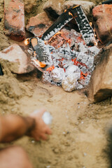 A person is standing over a fire pit, holding a can of lighter fluid