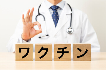 「ワクチン」と書かれたブロックとOKサインをする医師