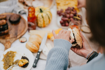 A woman is holding a sandwich in front of a table with a variety of food items