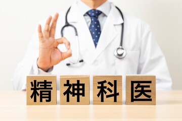 「精神科医」と書かれたブロックとOKサインをする医師