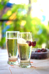 Refreshing, chilled summer beverage with water drops and cherries, set outdoors with a beautiful, bright green garden bokeh background