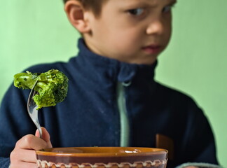 An Unhappy Boy Looking with Dislike at a Piece of Broccoli - A picky eater who dislikes vegetables