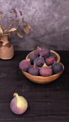 Fresh figs arranged in rustic wooden bowls with a single fig in front and vase decor softly blurred in the dark background