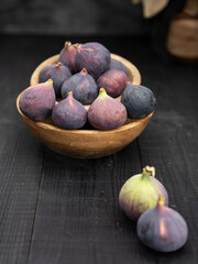 Two ripe figs in front with more in wooden bowls and a vase behind, captured in dark moody style on black wooden background
