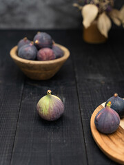Close up of ripe figs on a brown wooden plate and bowl against a dark background, styled with rustic tones and soft depth