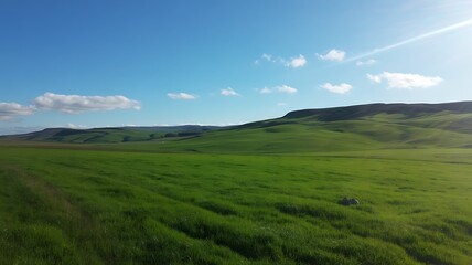 Fototapeta premium Expansive rolling green hills under a vast blue sky with wispy clouds