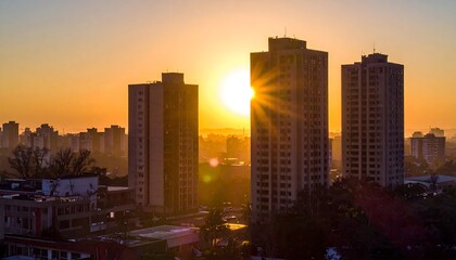 Obraz premium A stunning urban sunrise bathes tall buildings in golden light. Silhouettes of distant structures dot the horizon, creating a tranquil, yet expansive, city view
