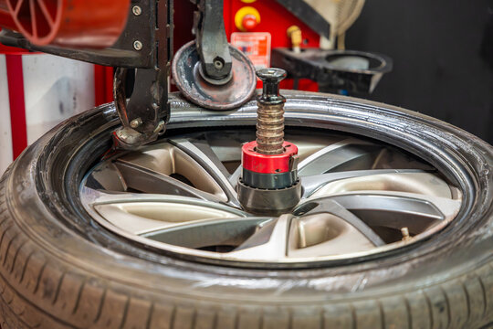 Tire changing machine removing the rubber tire from the rim using a rotating metal arm. Essential step in seasonal wheel replacement at a professional auto workshop.