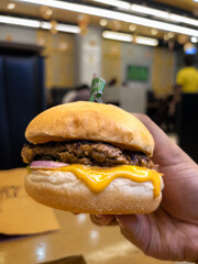 Close-up of a Hand Holding a Juicy Cheeseburger in a Restaurant