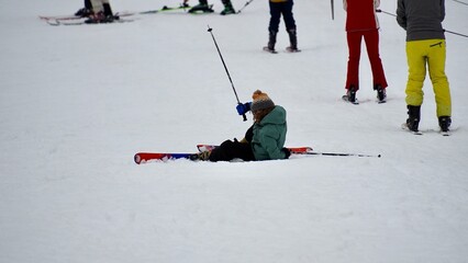 Young beginner skier falls on a snowy ski slope while learning to ski at a winter resort in the mountains