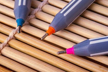 Three pens tip are featuring white stripes and brightly colored tips. Resting on a textured background made of parallel bamboo sticks tied together with twine. Selective focus.