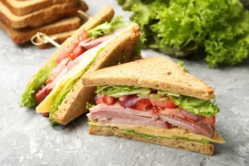 Delicious sandwiches with ham, cheese and vegetables on grey textured table, closeup