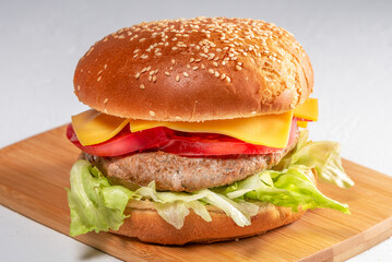 Juicy burger with cheddar cheese, lettuce, and tomato served on a sesame seed bun on a wooden...