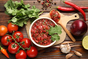 Delicious salsa sauce in bowl and ingredients on wooden table, flat lay