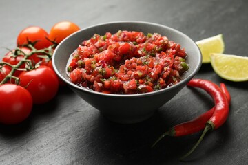 Delicious salsa sauce in bowl and ingredients on dark grey table, closeup
