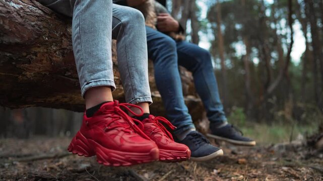 Sitting on log wearing red sneaker with friend resting legs dangling over forest floor shoe and foot close up showing casual hiking sneaker detail while trail leaf litter and nature surround