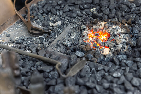 Close-up detail old medieval blacksmith furnace with hot burning coal flame forge iron metal. Craft smith farrier workshop fireplace with many professional craftsman tools equipment