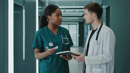 medical professionals in discussion inside a modern hospital, a female nurse in green scrubs with a stethoscope around her neck holding a clipboard, speaking to a doctor - Powered by Adobe