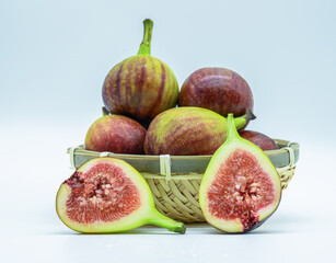 흰색 배경의 바구니에 담긴 무화과와 반쪽의 무화과 