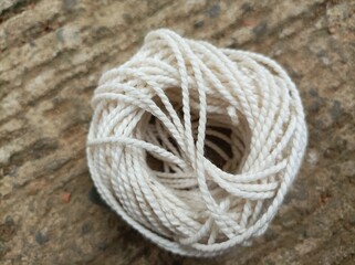 ball of string, A white yarn ball placed on a rough concrete surface under natural light, showing fine texture, soft tones, and aesthetic composition in close-up view.