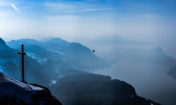 Crucifix on a mountain peak with a bird flying in the distance, Switzerland