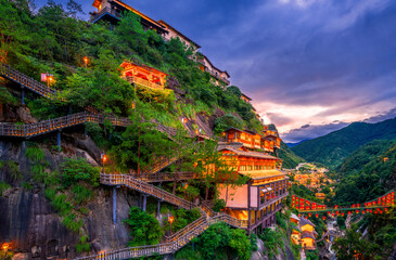 Traditional Chinese style buildings and wooden stairways clinging to a steep cliffside in a mountain village at dusk in Jiangxi, China.