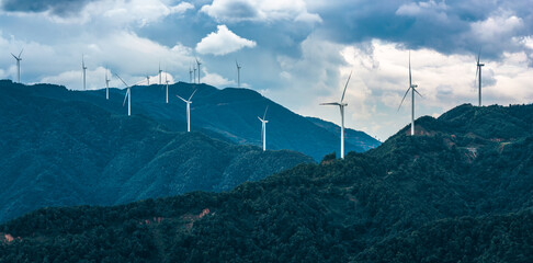A large wind farm with rows of modern wind turbines generating clean renewable energy on top of green mountains.