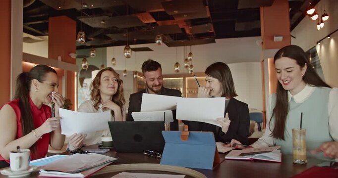 Business team meeting in a cafe, discussing positive results. They are smiling, laughing, and enjoying their teamwork.