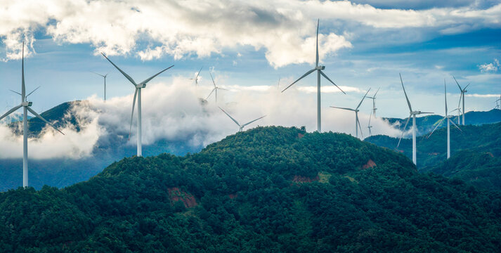 A large wind farm with multiple turbines on a series of green mountain ridges.