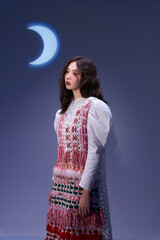 A woman in a colorful patterned dress poses gracefully against a soft moonlit background.