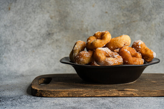 Close-up of a bowl of homemade donuts dusted with icing sugar on a wooden chopping board