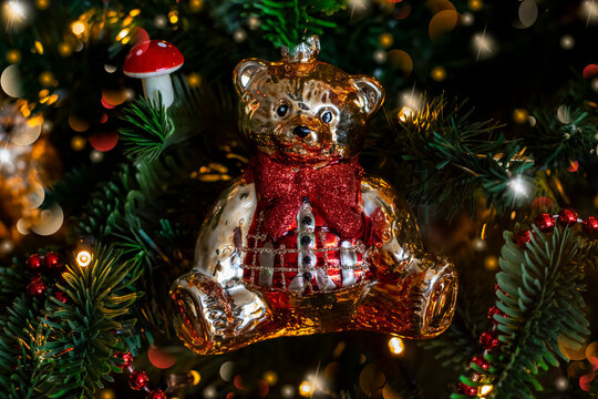 Teddy bear decoration on Christmas tree with festive lights garland, selective focus