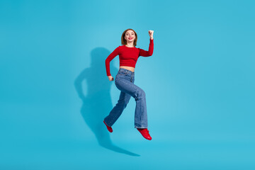 Fototapeta premium Lovely young woman in casual style jumps excitedly on a blue background wearing red shirt and jeans