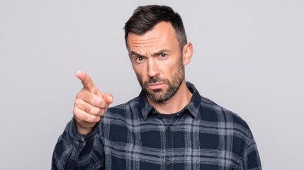 Fototapeta premium Serious Man in Casual Shirt Pointing with Confident Expression Against Neutral Background